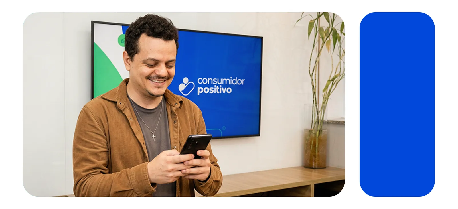 Homem sorrindo enquanto olha o celular, em frente a uma tela com o logo da Consumidor Positivo