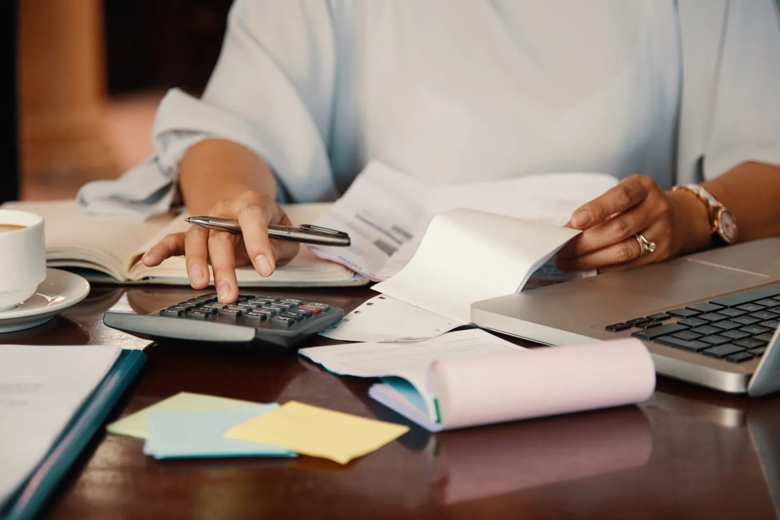 Pessoa fazendo contas na calculadora com boletos e notebook sobre a mesa